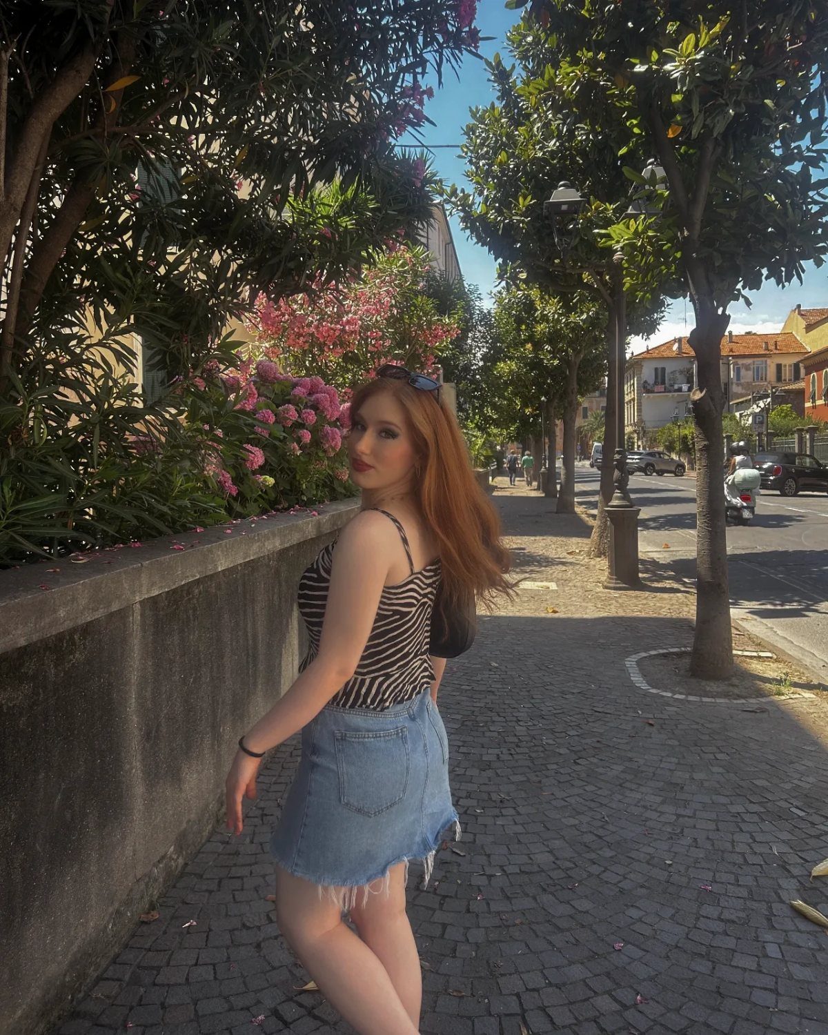 Woman in striped top and denim skirt posing on a sunny cobblestone street.