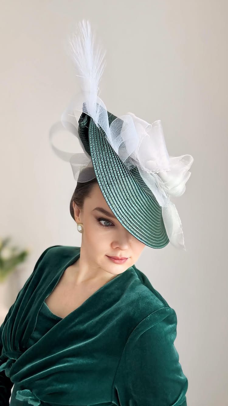 Woman in a green velvet dress wearing a large green and white decorative fascinator hat.