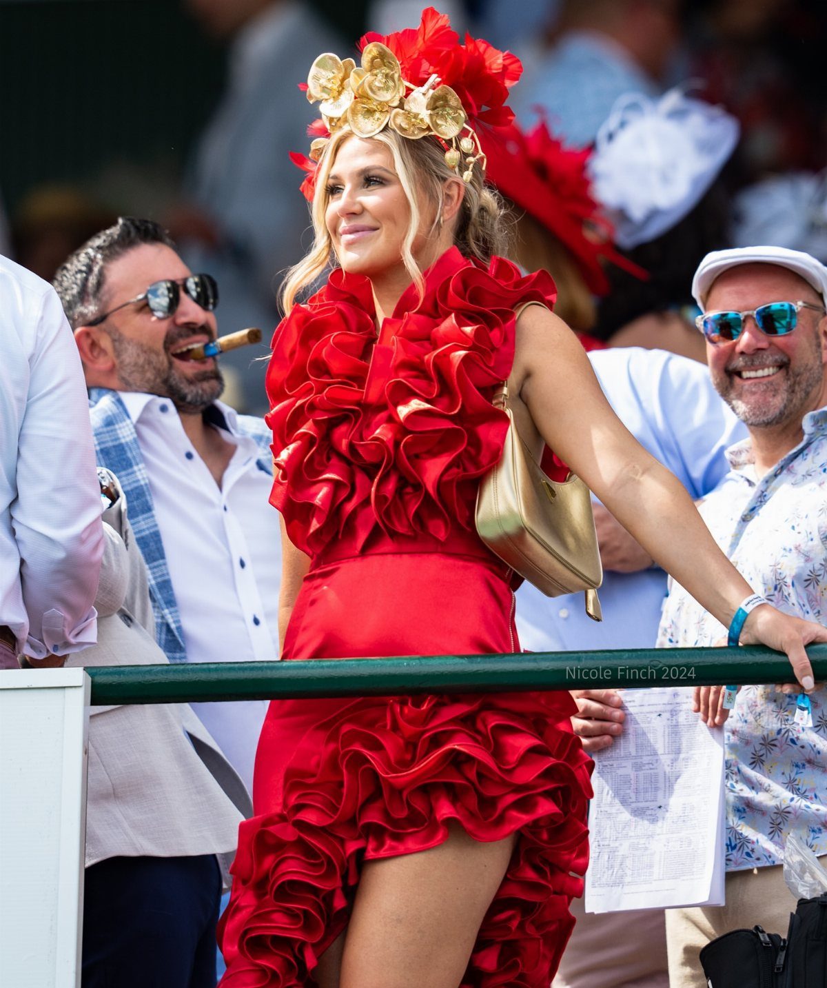 Woman in a bright red ruffled dress and large floral headpiece smiling in a crowd.
