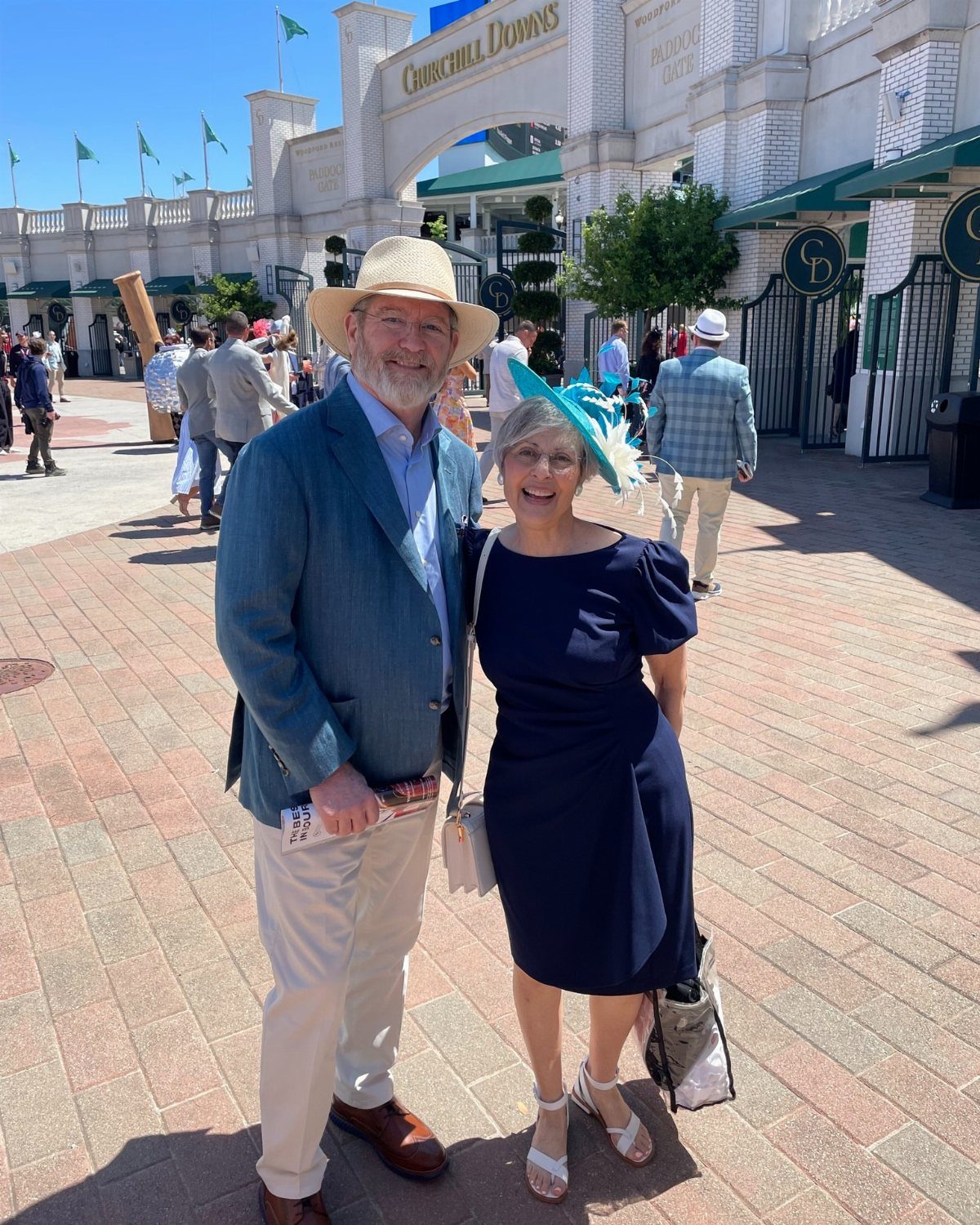 A man in a blue blazer and straw hat posing with a woman wearing a navy dress and turquoise fascinator.