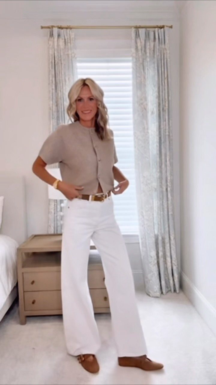 Woman posing in a beige shirt and white wide-leg trousers with brown loafers.