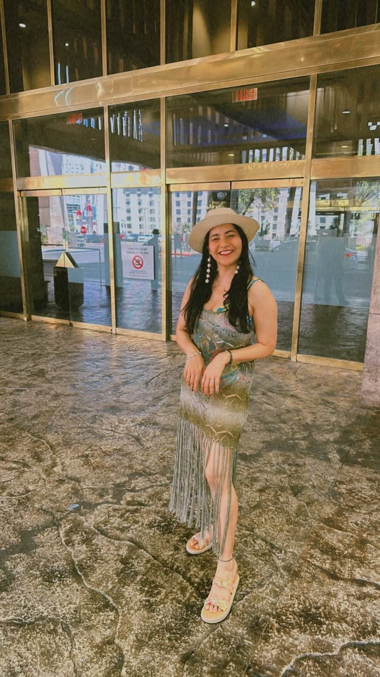 Smiling woman in a patterned fringe maxi dress and wide-brimmed hat standing outdoors.