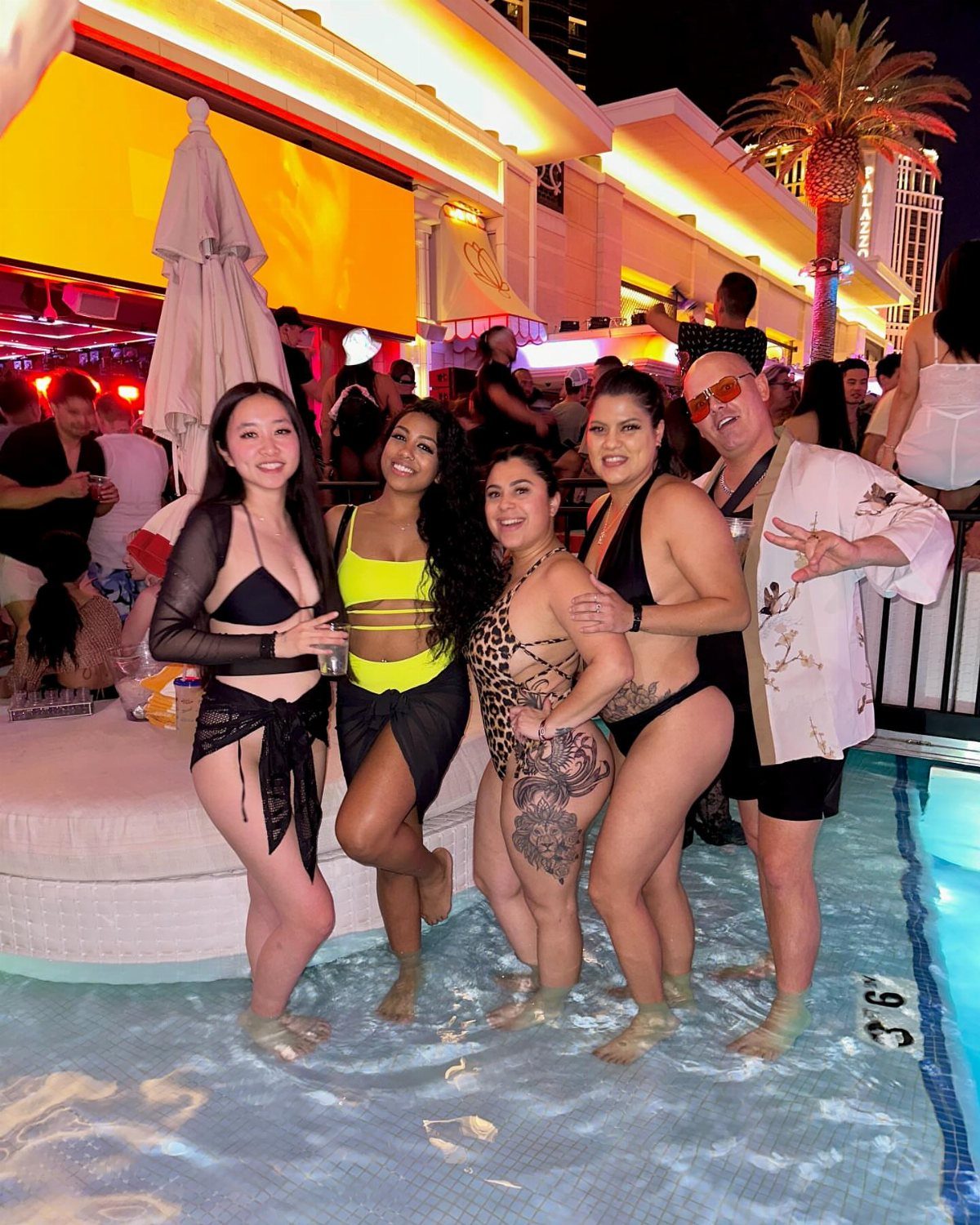 Five friends posing together in a shallow swimming pool at a night club.
