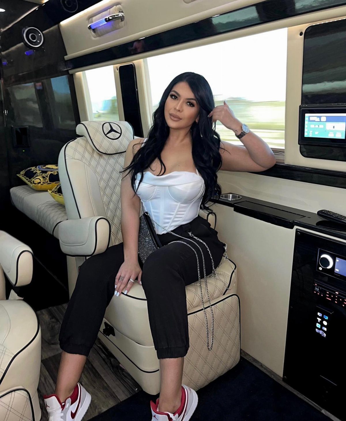 Woman in a white corset and black joggers sitting in a luxury vehicle seat.
