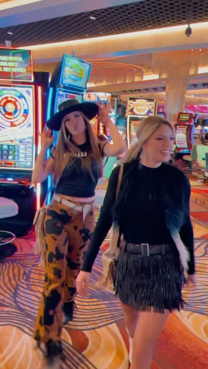 Two women in stylish western-inspired outfits walking through a brightly lit casino floor.