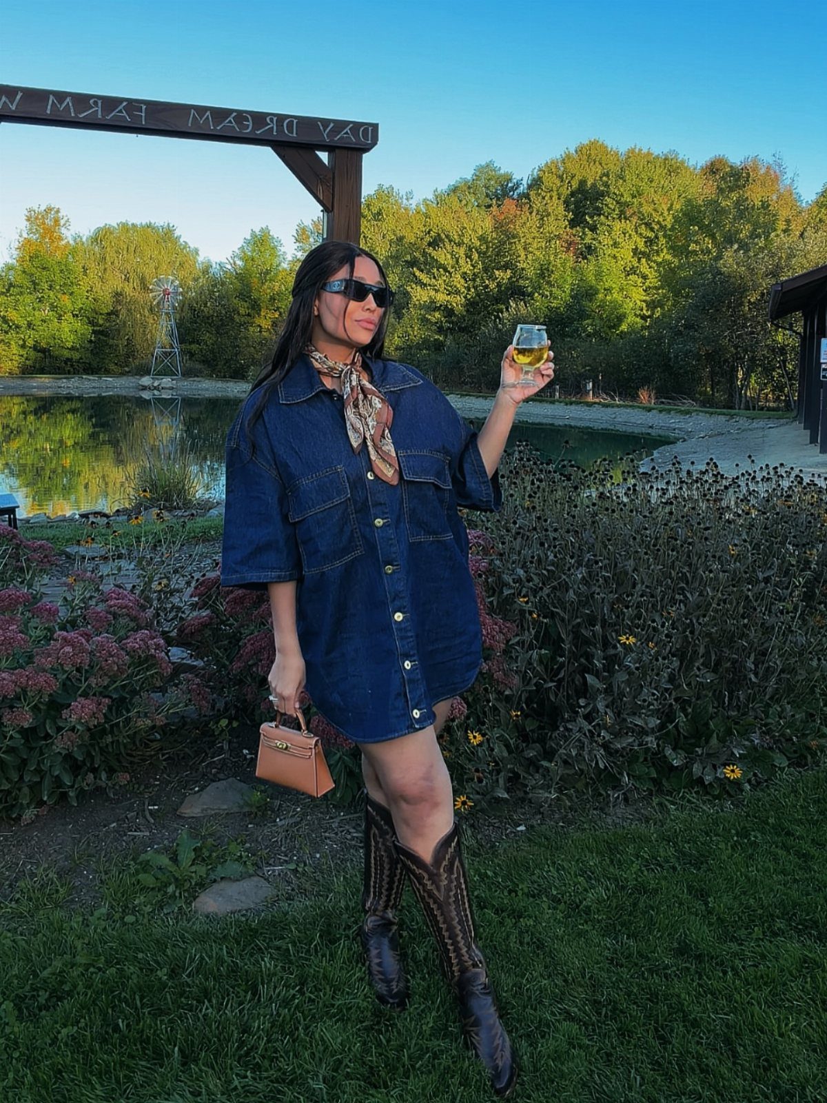 Woman in a denim shirt dress and embroidered cowboy boots standing in a garden.