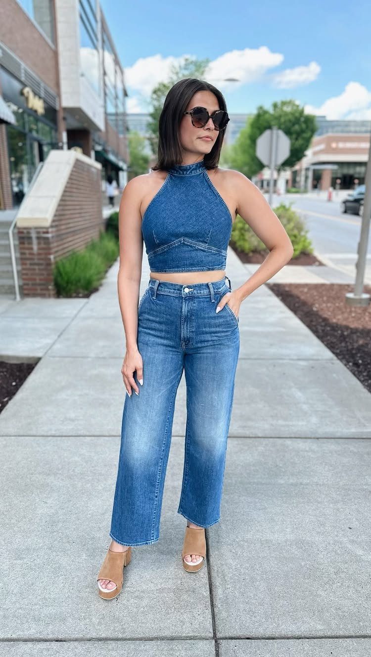 A woman posing in a blue denim halter crop top and matching wide-leg denim jeans on a city sidewalk.