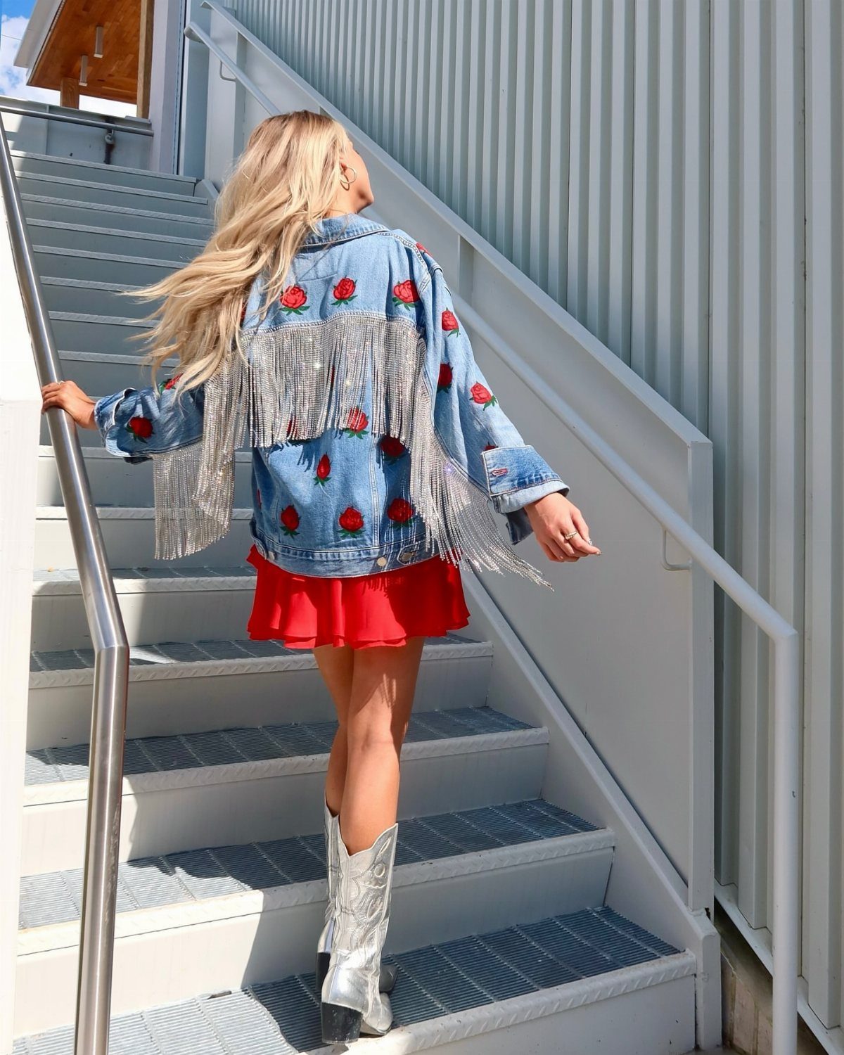 Blonde woman in a fringed denim jacket and silver cowboy boots walking up stairs.