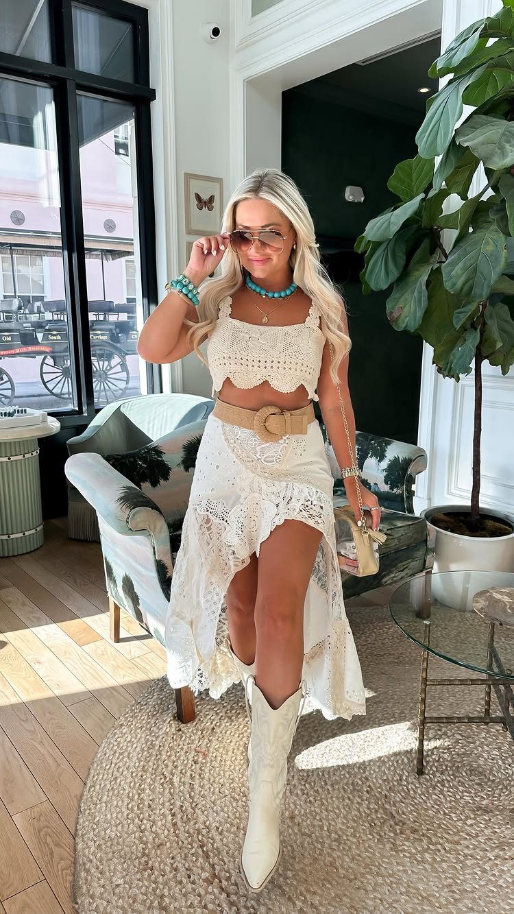 A blonde woman posing in a white lace outfit and white cowboy boots.
