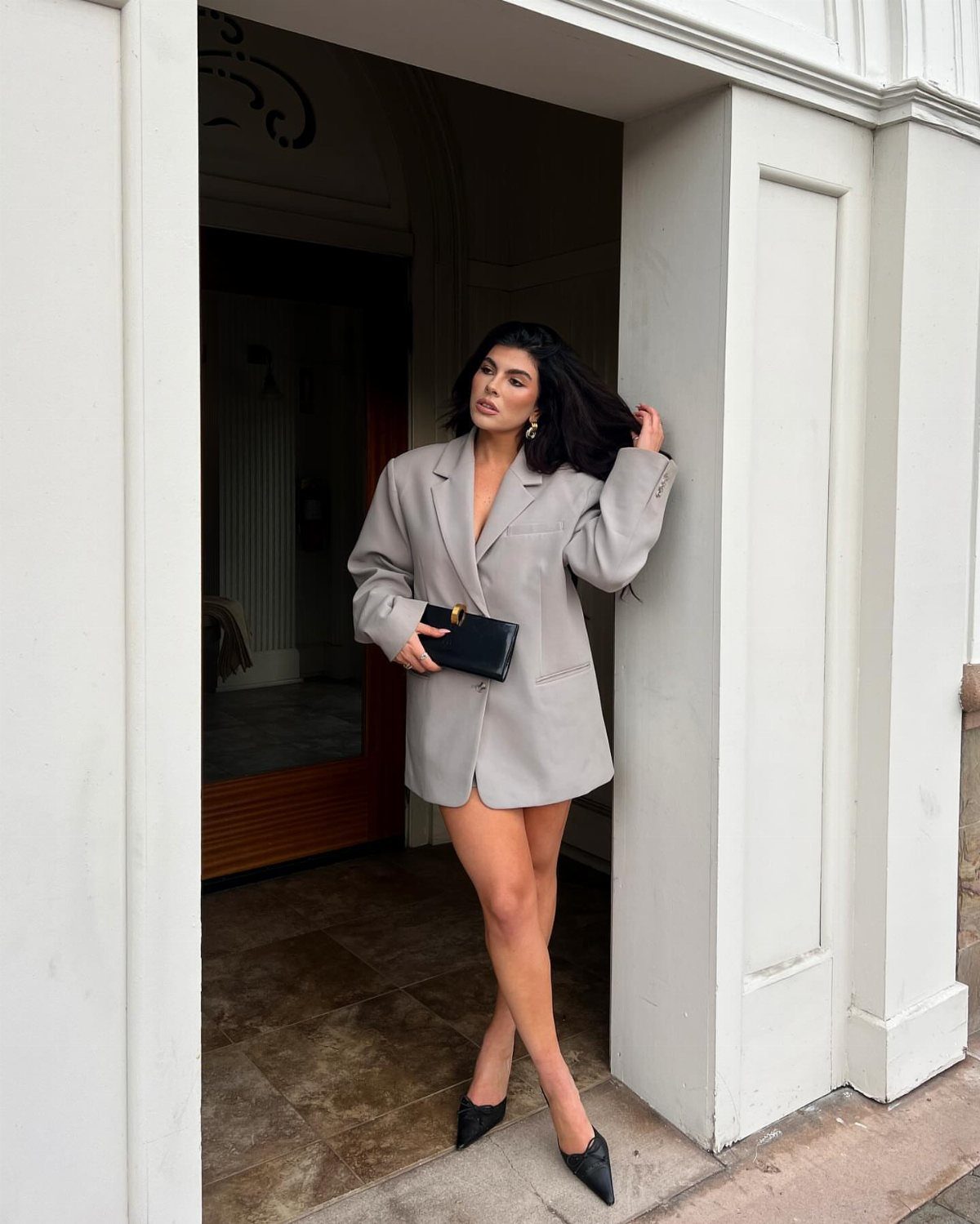 Woman posing in an oversized light grey blazer dress and black heels.