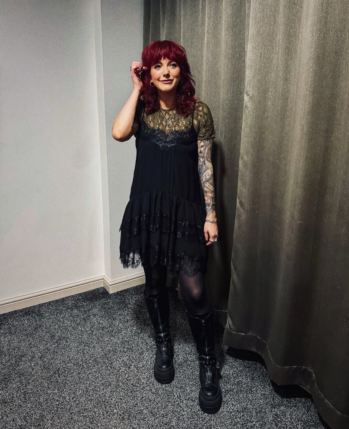 Woman with red hair wearing a black lace dress, black tights, and platform boots.