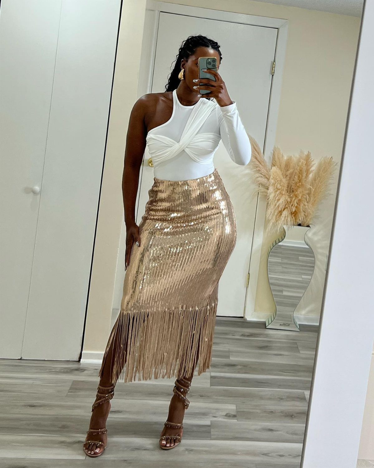 Woman in a white one-shoulder top and gold sequined fringe midi skirt posing in a mirror.