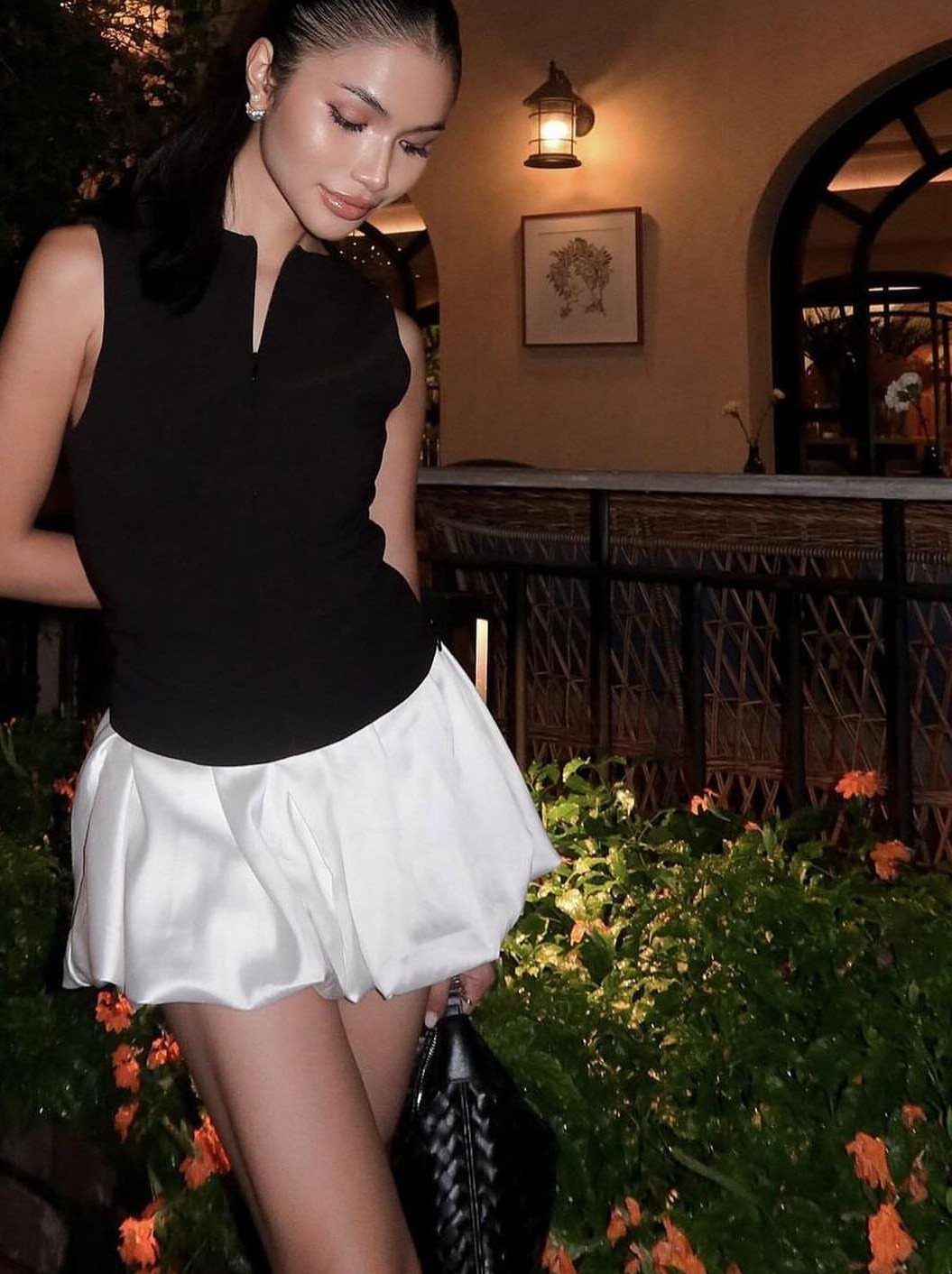Woman wearing a black sleeveless top and a white voluminous bubble skirt outdoors at night.
