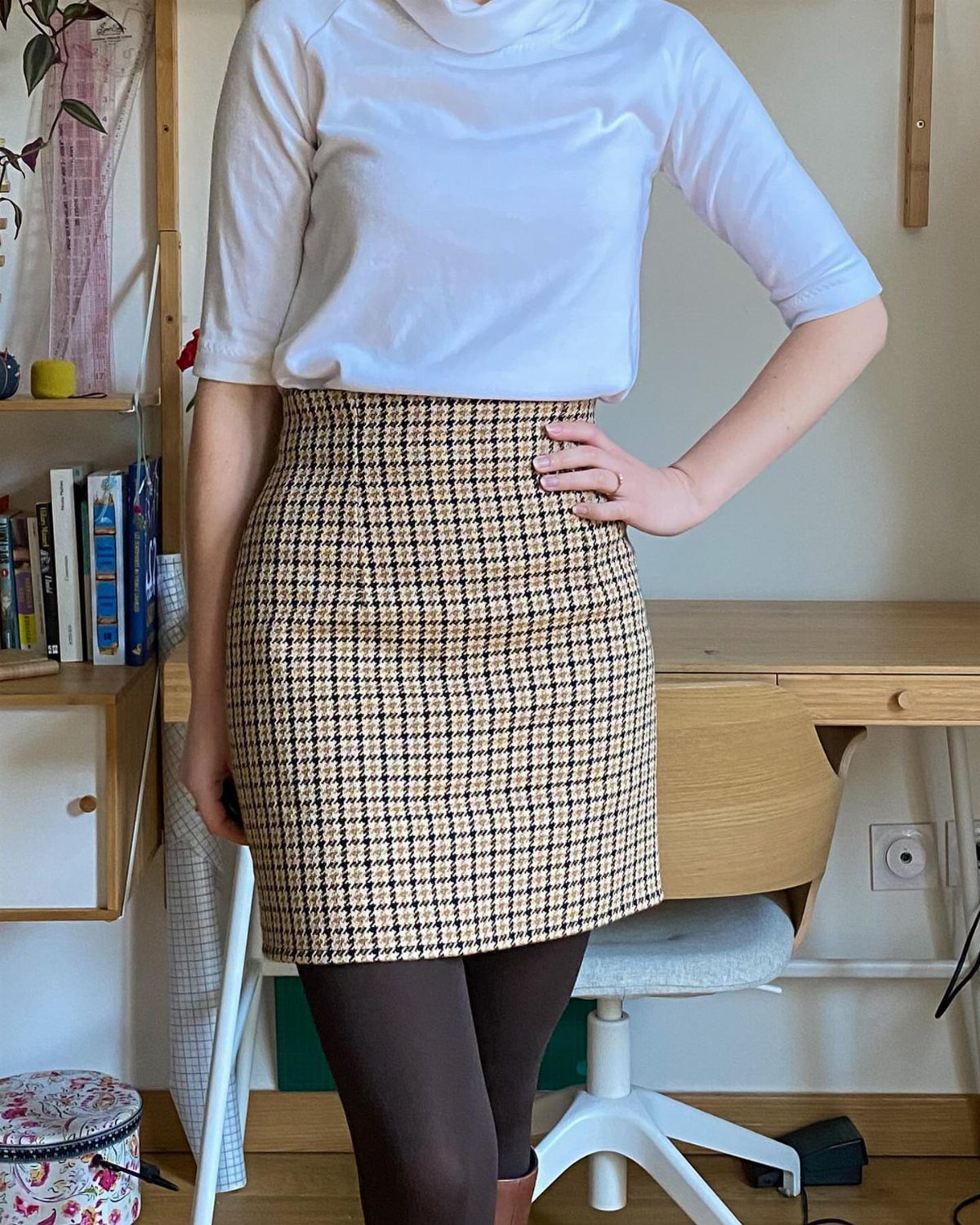 A person wearing a white top and a patterned high-waisted pencil skirt with dark tights.