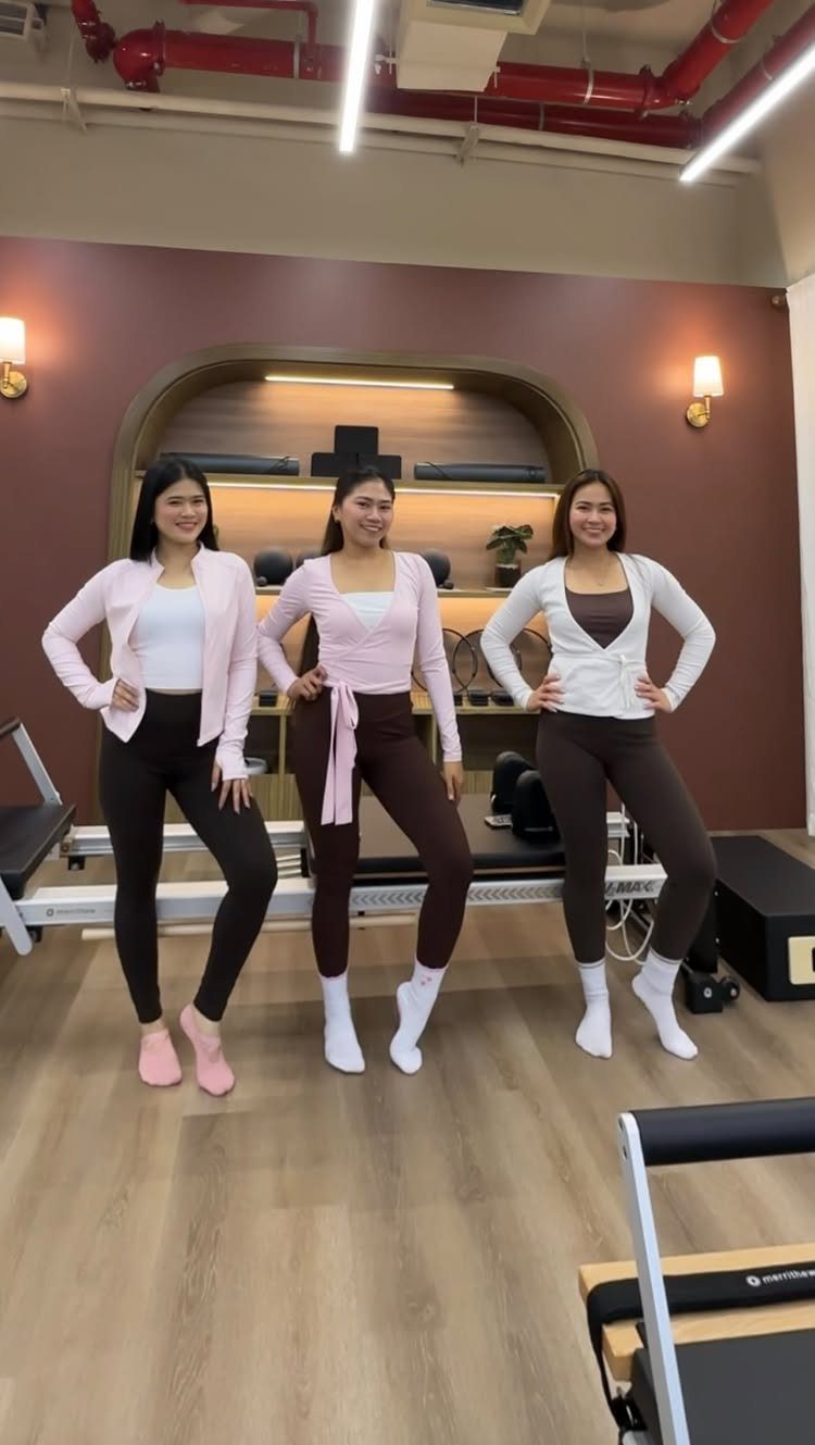 Three women posing in a pilates studio wearing stylish athleisure outfits and leggings.