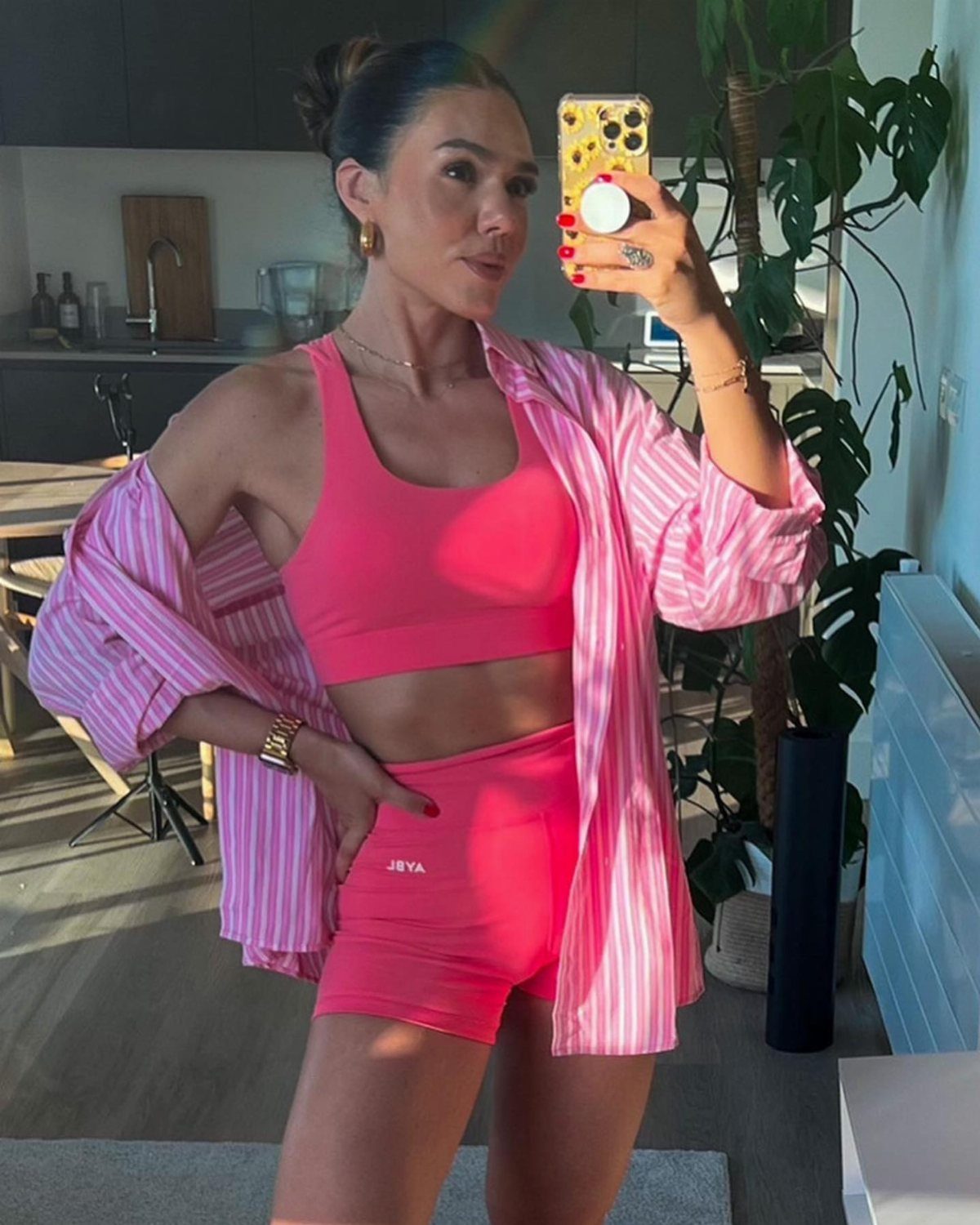 Woman in a pink sports bra and matching biker shorts posing for a mirror selfie.