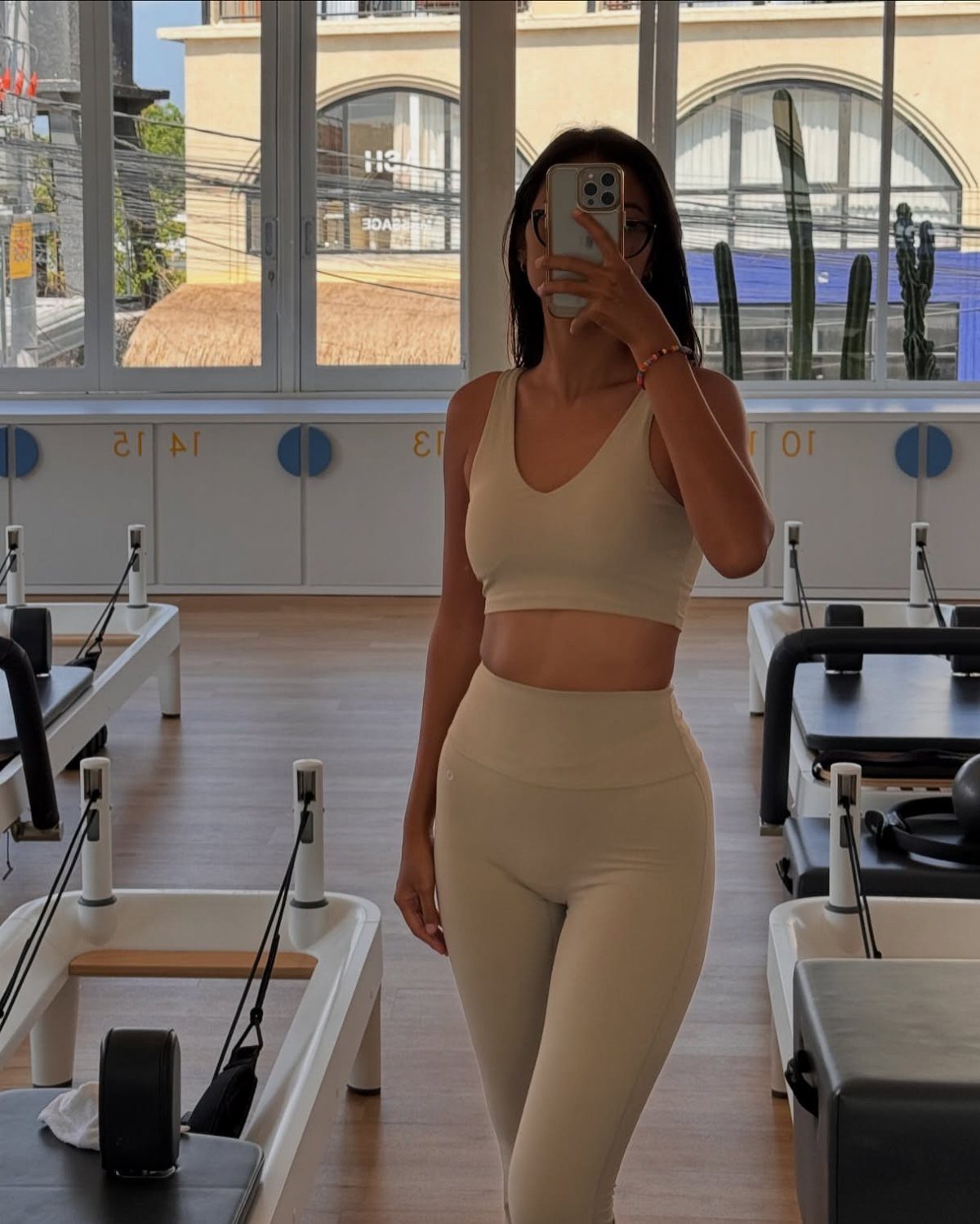 Woman in a beige matching athletic set posing in a pilates studio.