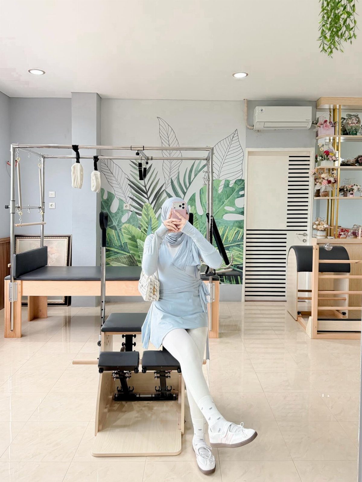 Woman in light blue athletic wear and white leggings posing in a pilates studio.