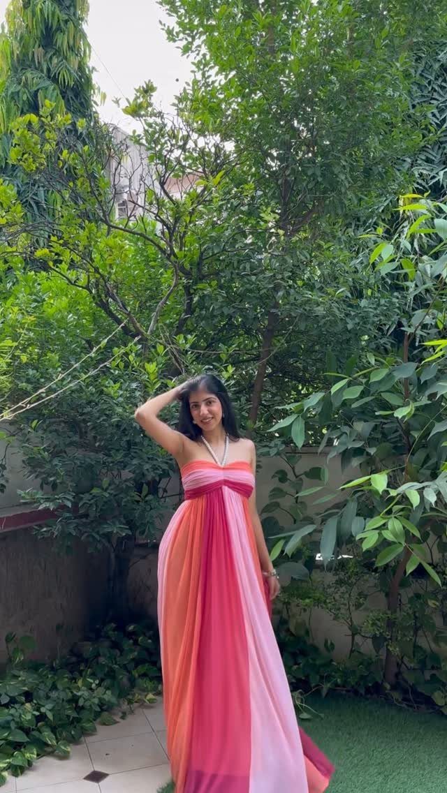 A woman in a colorful striped strapless maxi dress posing in a green garden.