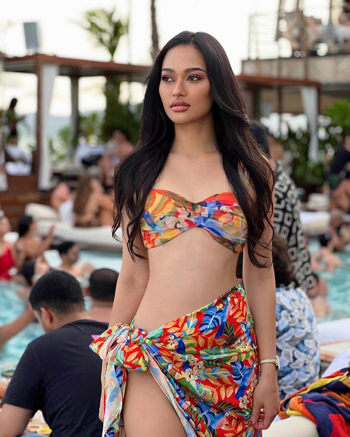 A woman wearing a colorful tropical print bikini and matching wrap skirt by a pool.