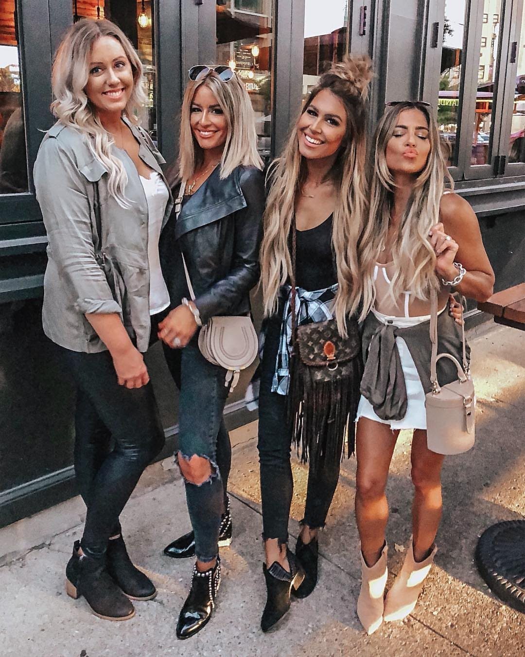 Four women posing together outdoors, one wearing a black leather jacket and ripped jeans.