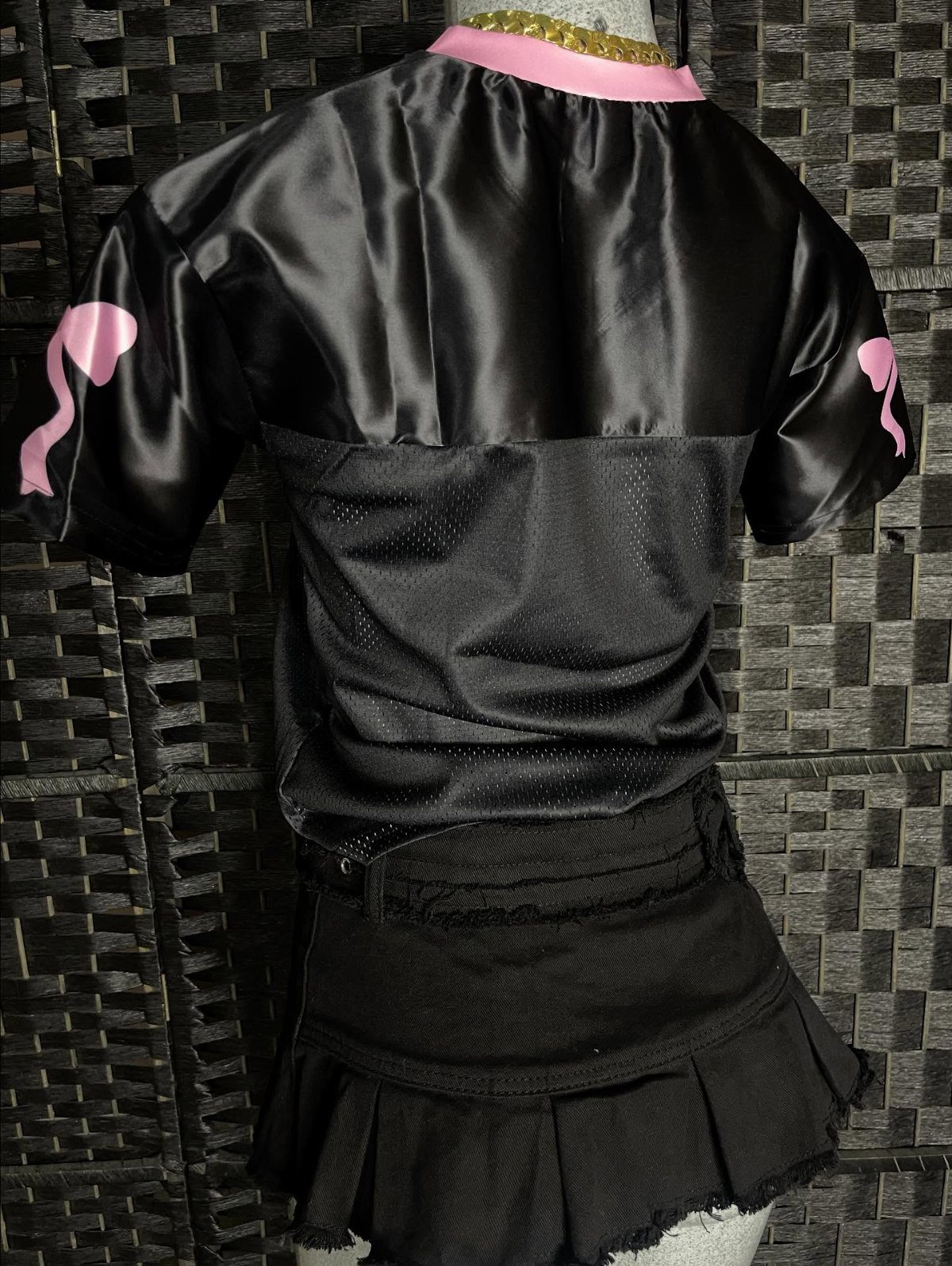 Black pleated mini skirt and satin top displayed on a mannequin against a dark textured wall.