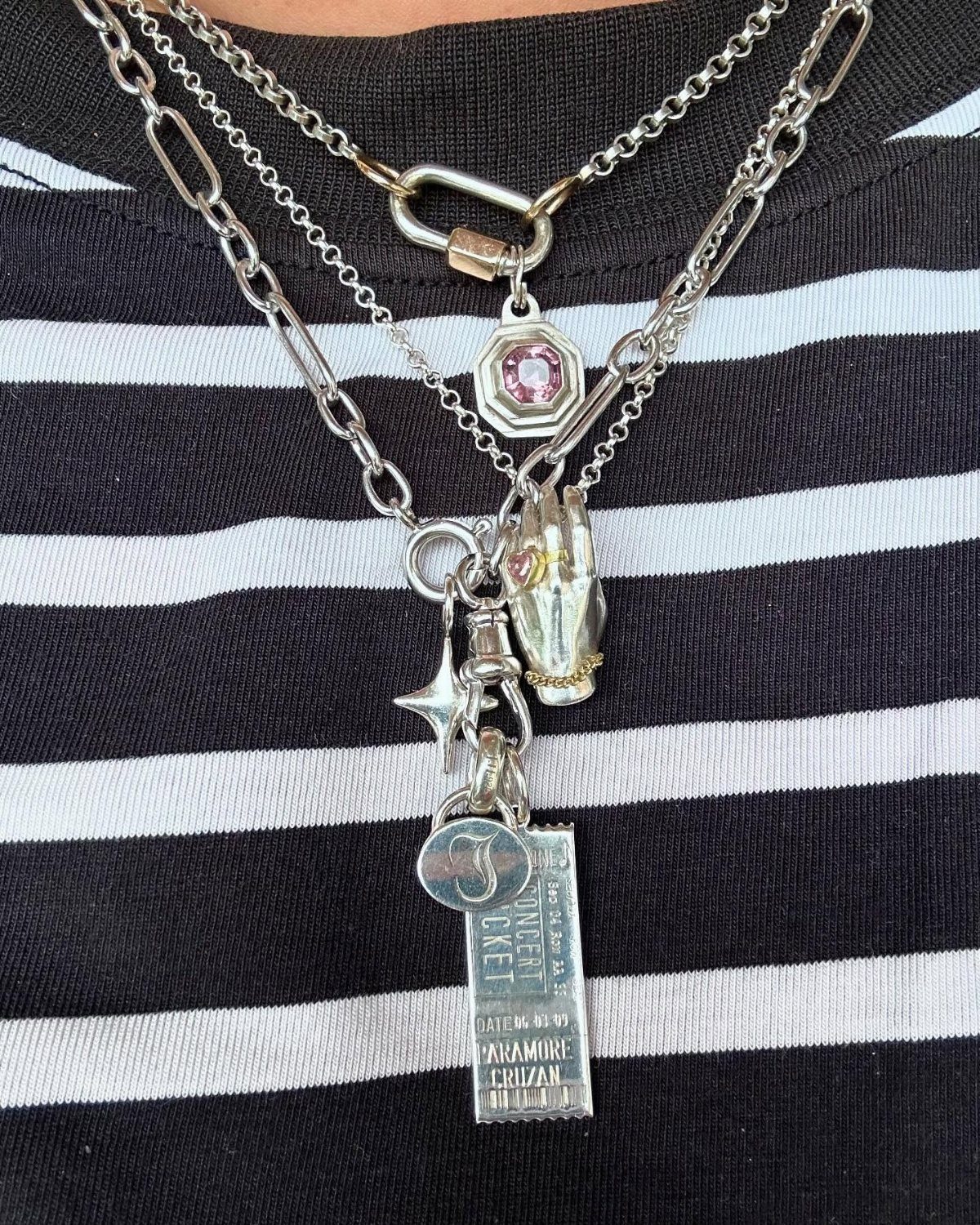 Silver layered necklaces with various charms worn over a black and white striped shirt.
