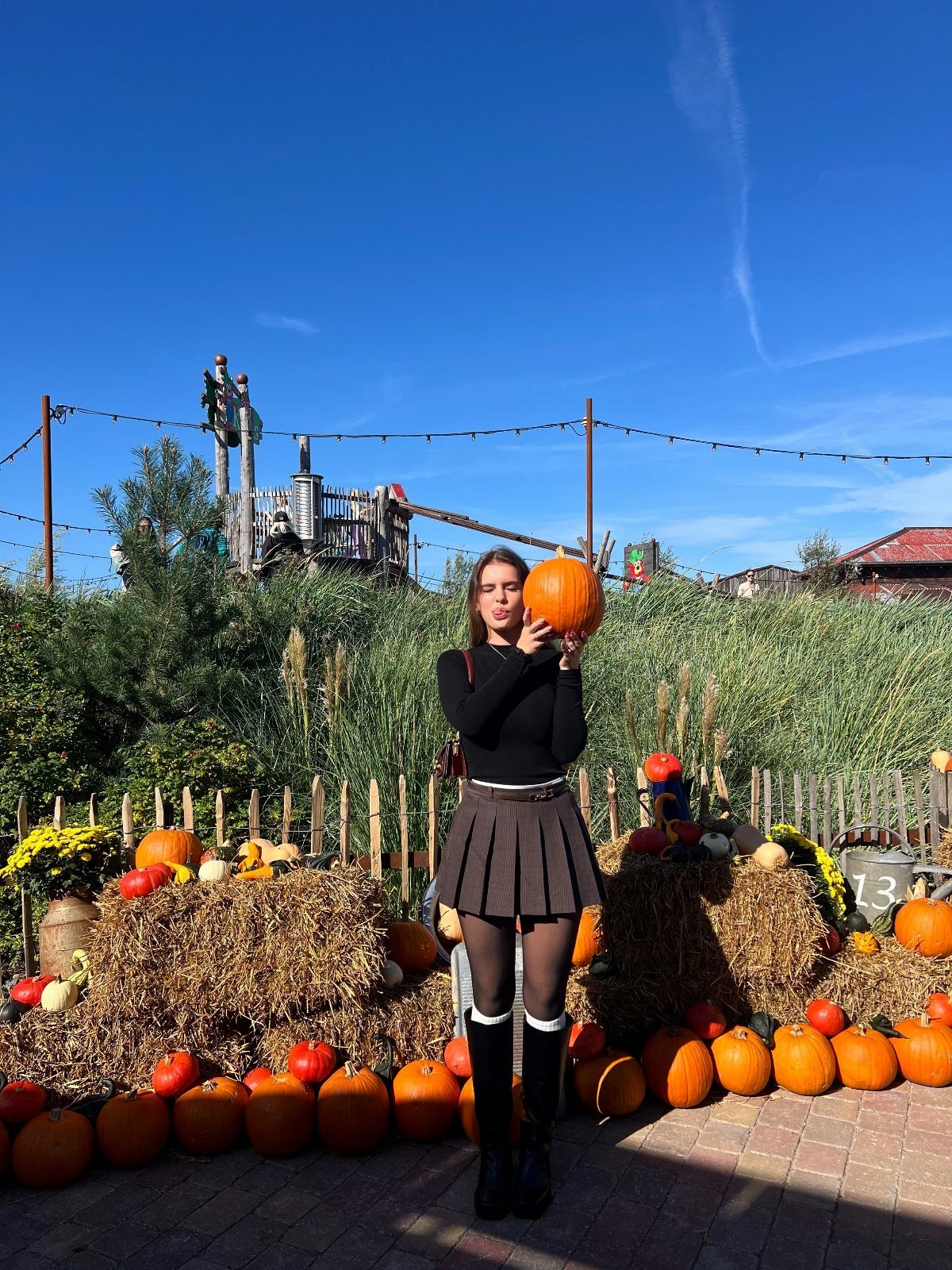 Woman in black top and plaid skirt holding a pumpkin in a field.