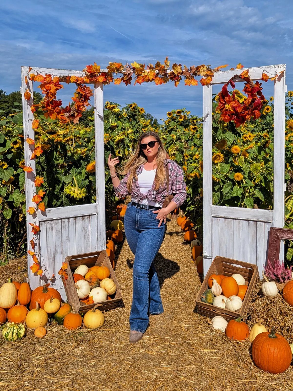 Woman in a plaid flannel shirt and blue jeans posing in a pumpkin patch.