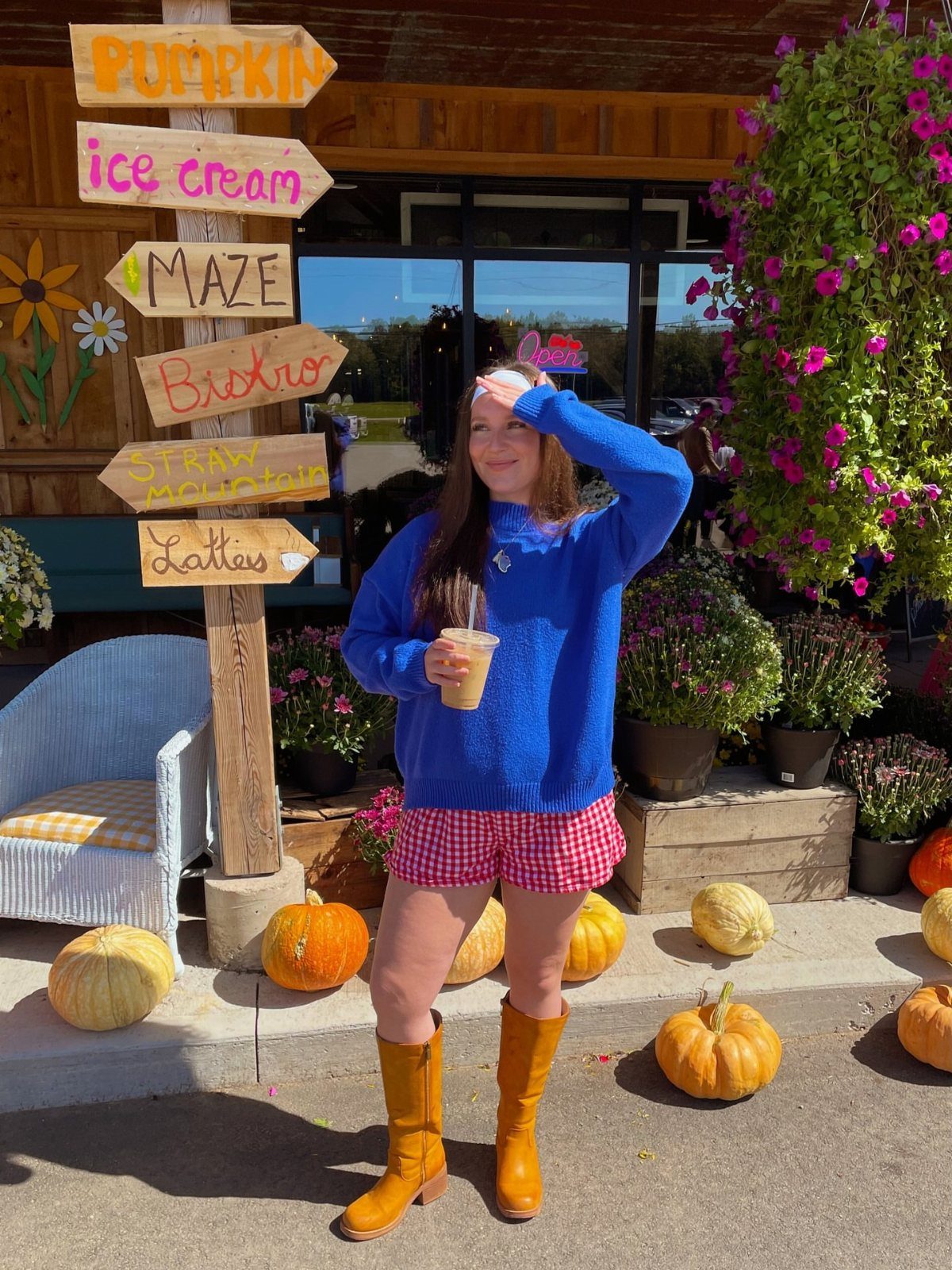Woman in a blue sweater and red checkered ruffled shorts standing near pumpkins.