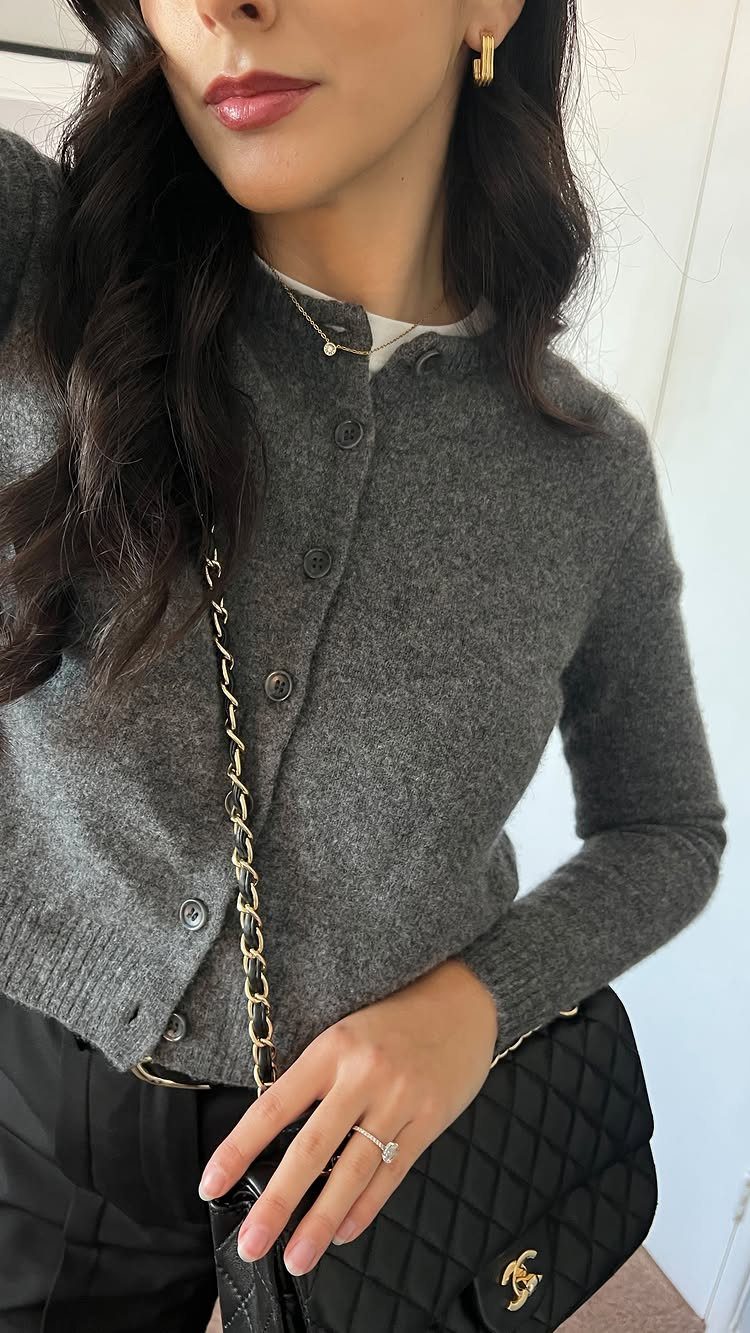 A woman wearing a grey buttoned cardigan over a white top and black trousers.