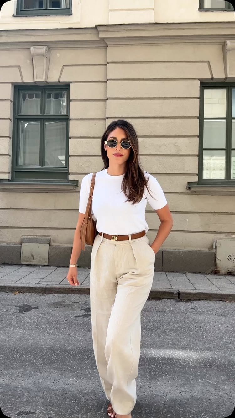 Woman posing in a white t-shirt, beige trousers, and sunglasses on a city street.