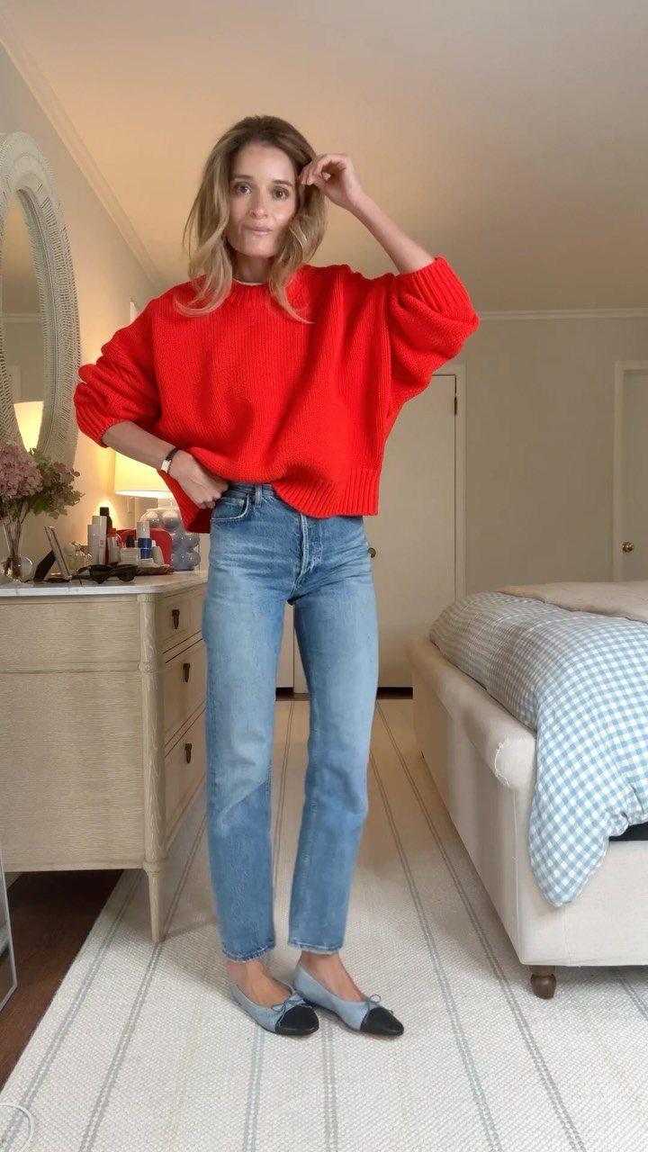 Woman posing in a bright red sweater and light blue denim jeans.