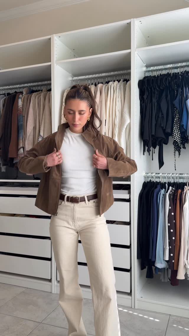 Woman wearing a white t-shirt, brown jacket, and cream wide-leg jeans in a closet.