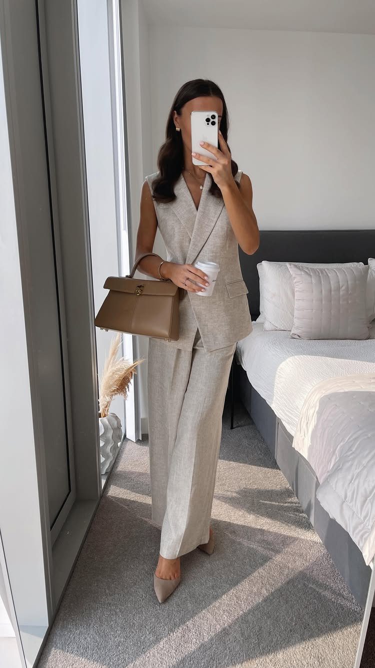 Woman in a beige linen vest and wide-leg trousers holding a brown handbag.