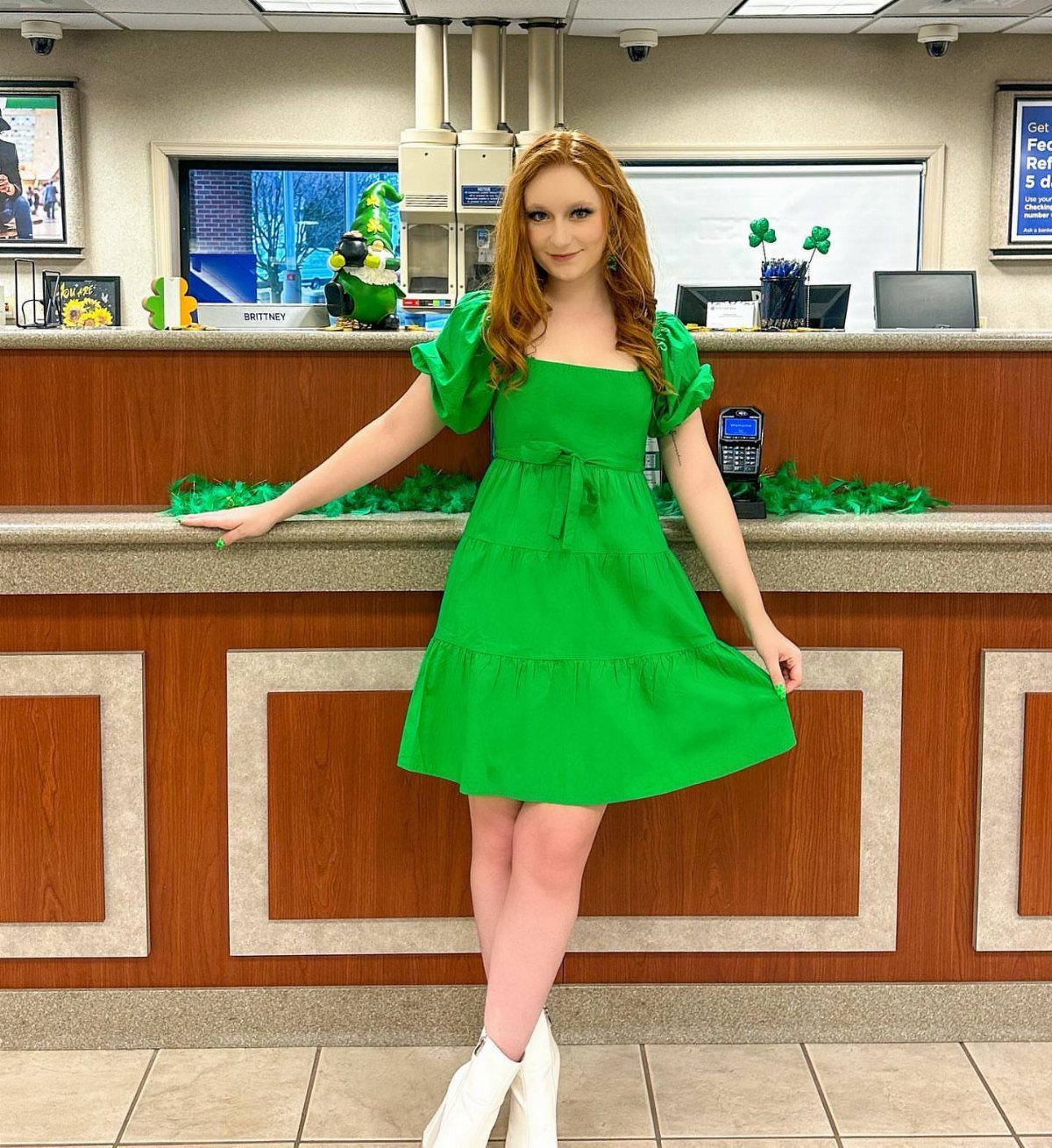Red-haired woman posing in a bright green tiered dress standing in front of a counter.