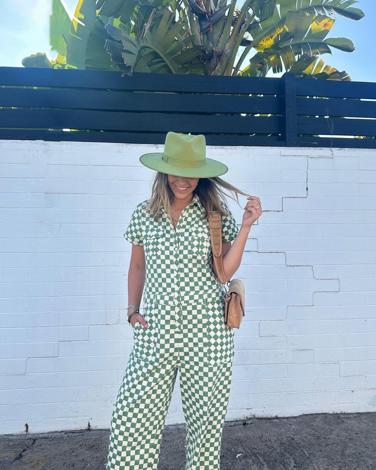 Woman posing in a green and white checkered jumpsuit and a matching green wide-brimmed hat.