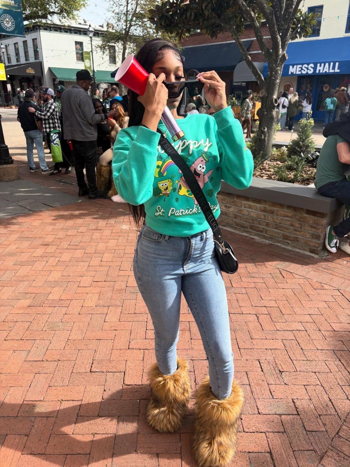 Woman in a green graphic sweatshirt, light blue jeans, and tan furry boots standing outdoors.