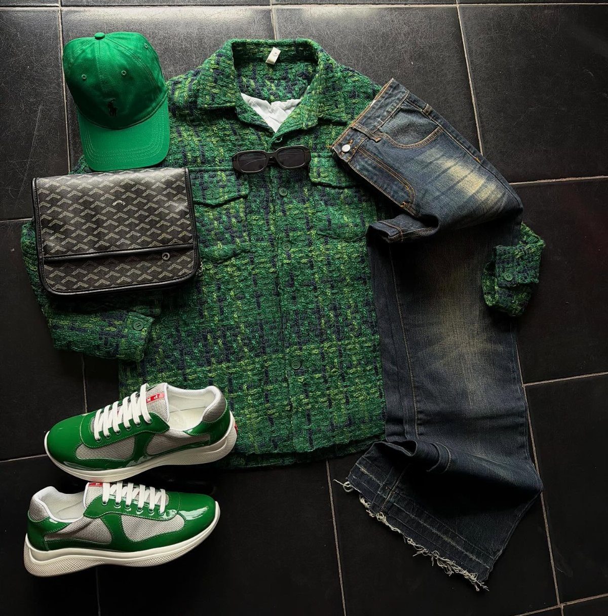 Green textured shirt, denim jeans, green sneakers, and a green cap laid on dark tiles.