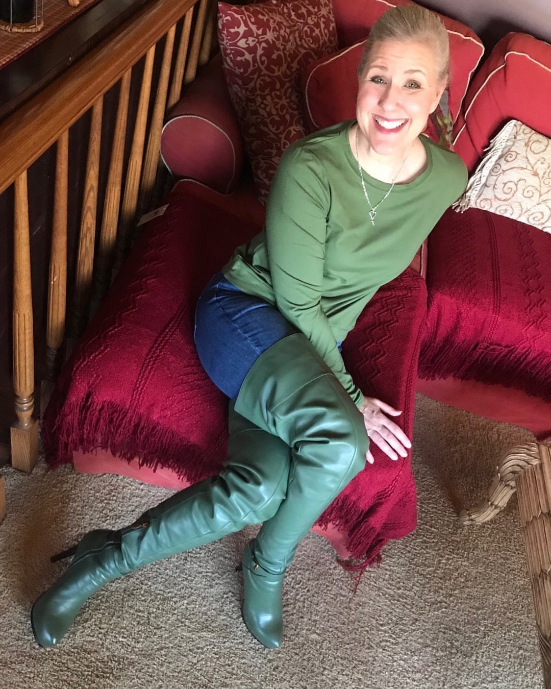 Smiling woman sitting on a red sofa wearing a green top, denim shorts, and green boots.