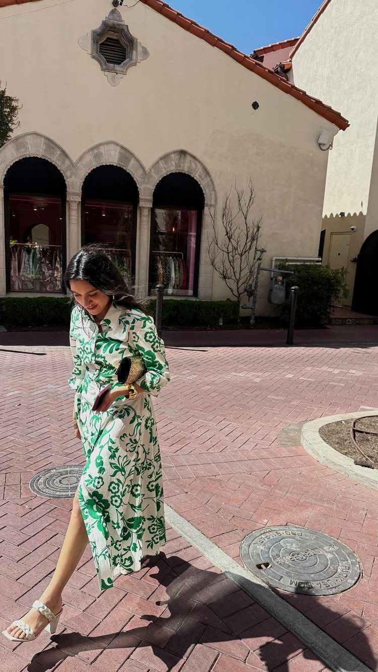 Woman walking in a white and green floral patterned maxi dress and white sandals.