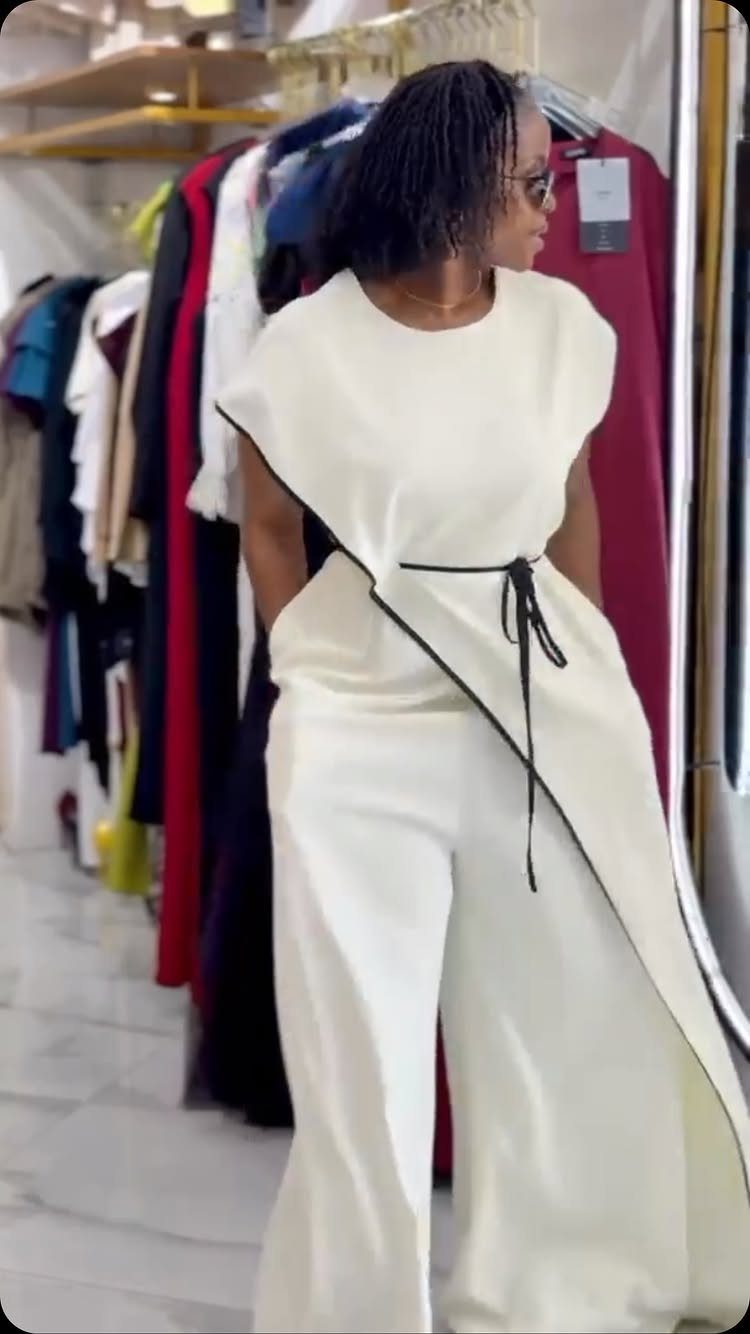 Woman wearing a white wide-leg jumpsuit with black trim standing in a clothing boutique.