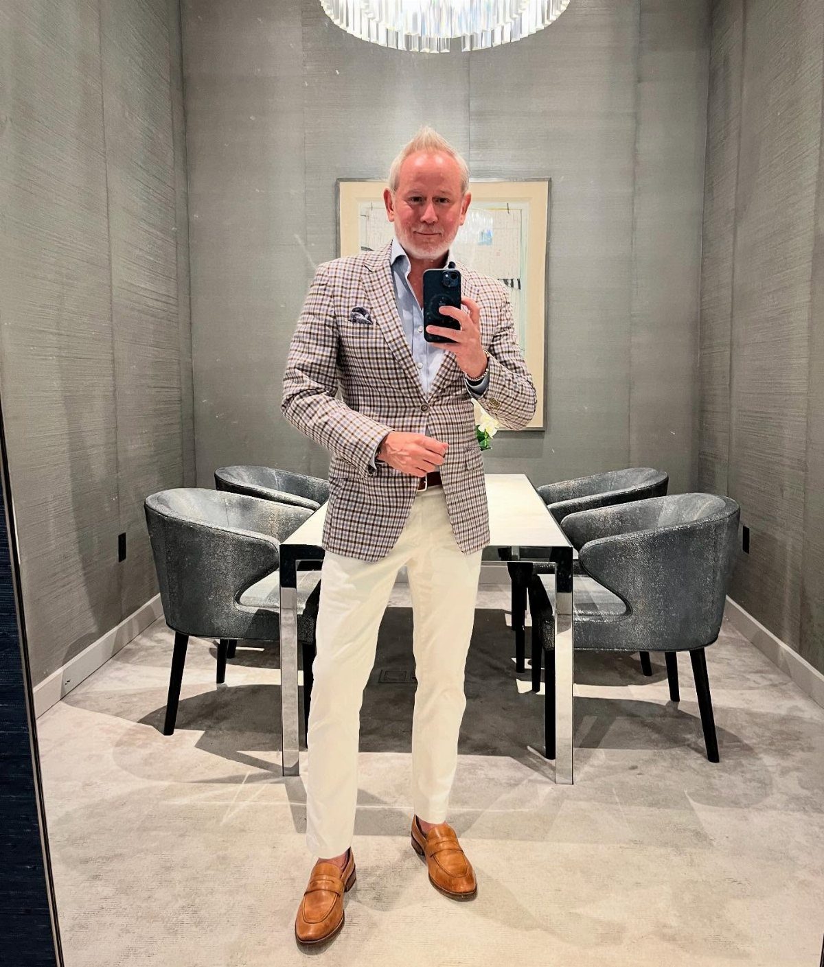 Man in a patterned blazer, light blue shirt, white trousers, and brown loafers posing for a selfie.