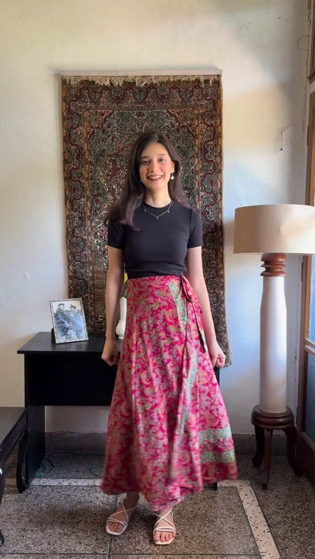 A woman smiling in a black t-shirt and a long pink patterned wrap skirt.