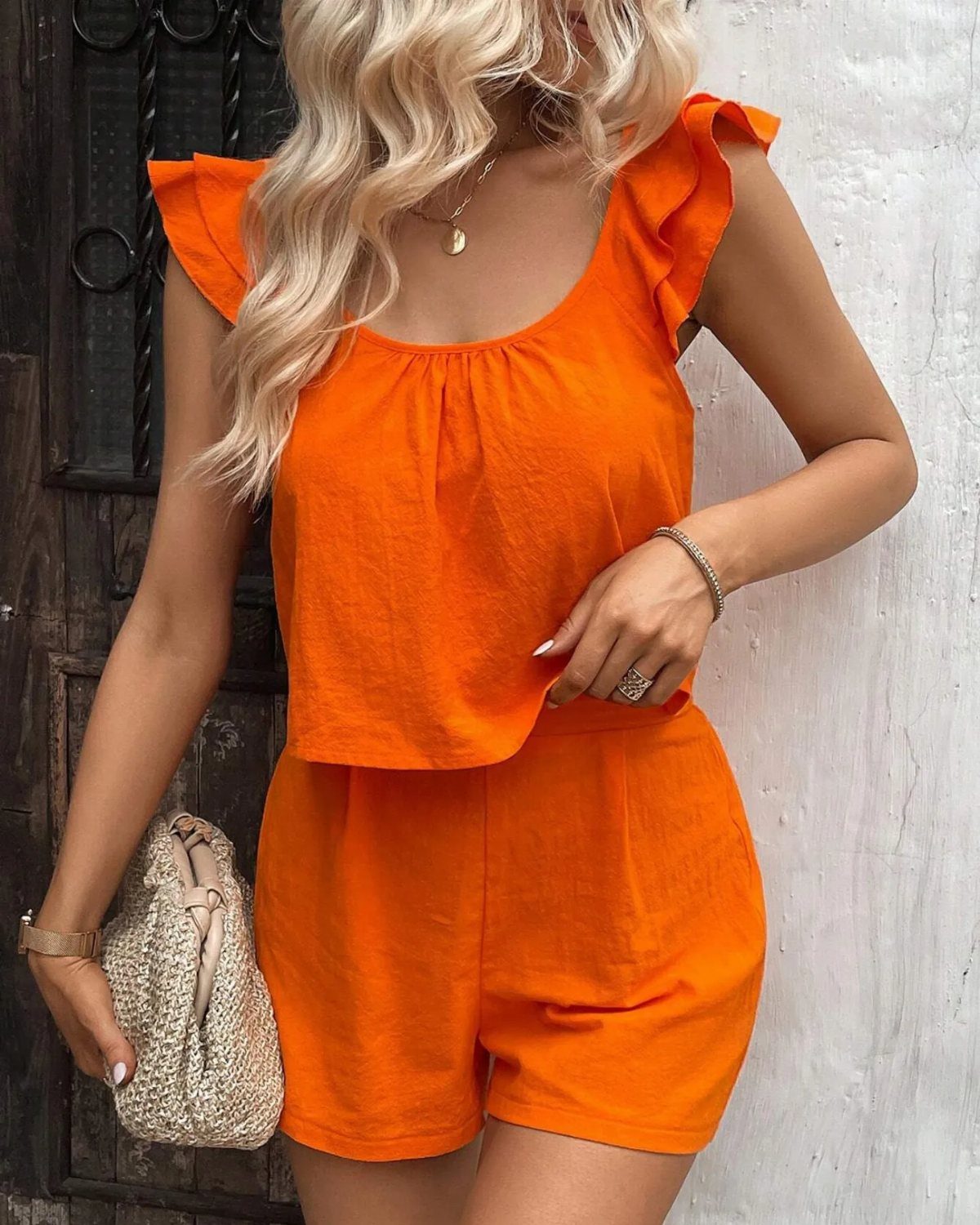 Blonde woman posing in a bright orange ruffled sleeveless top and matching summer shorts.