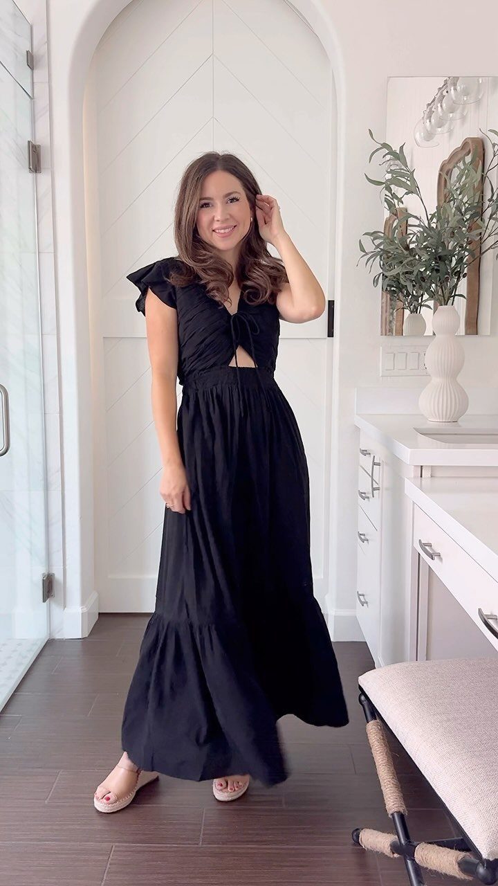 Woman posing in a black sleeveless maxi dress with a cutout waist in a bright room.