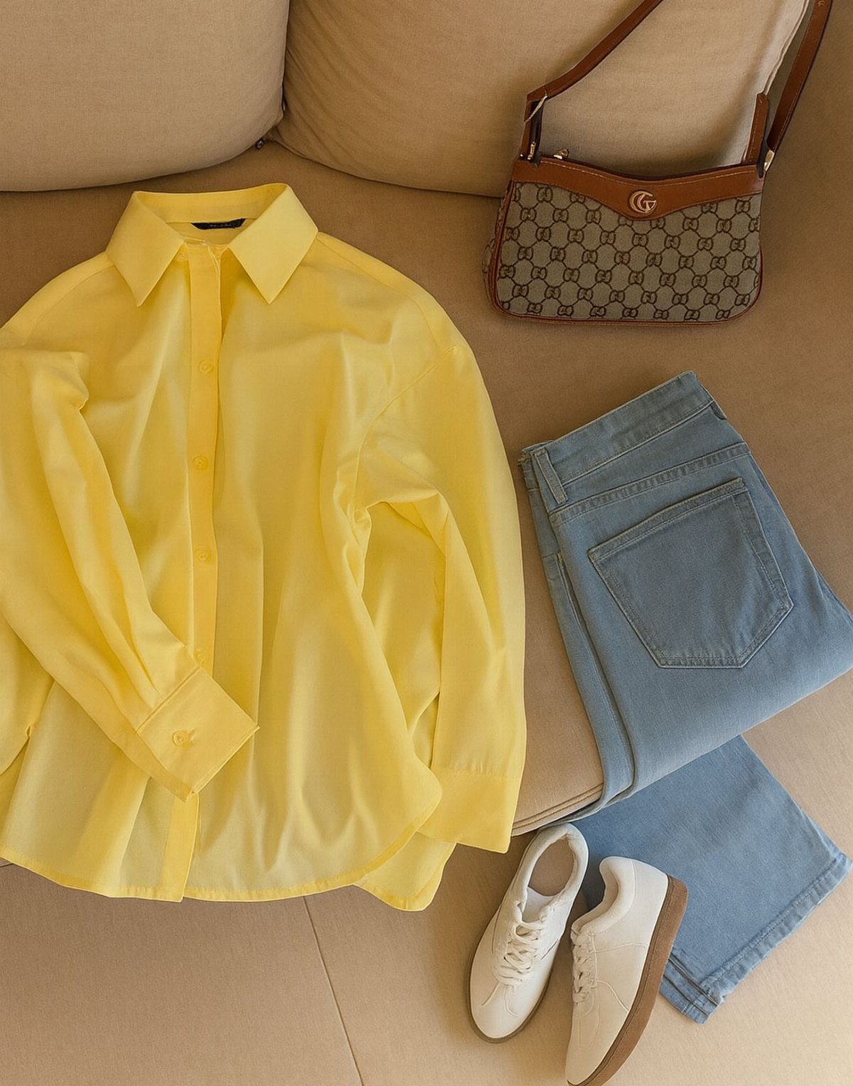 Yellow button-down shirt, blue jeans, white sneakers, and a patterned handbag laid out as a summer outfit.