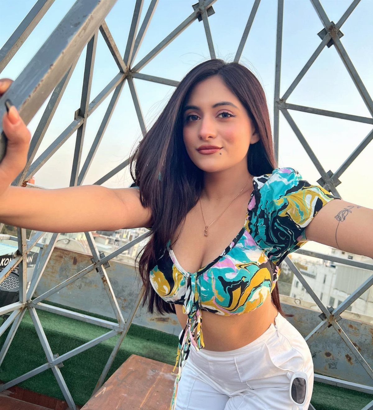 A young woman wearing a colorful patterned crop top and white pants posing outdoors.