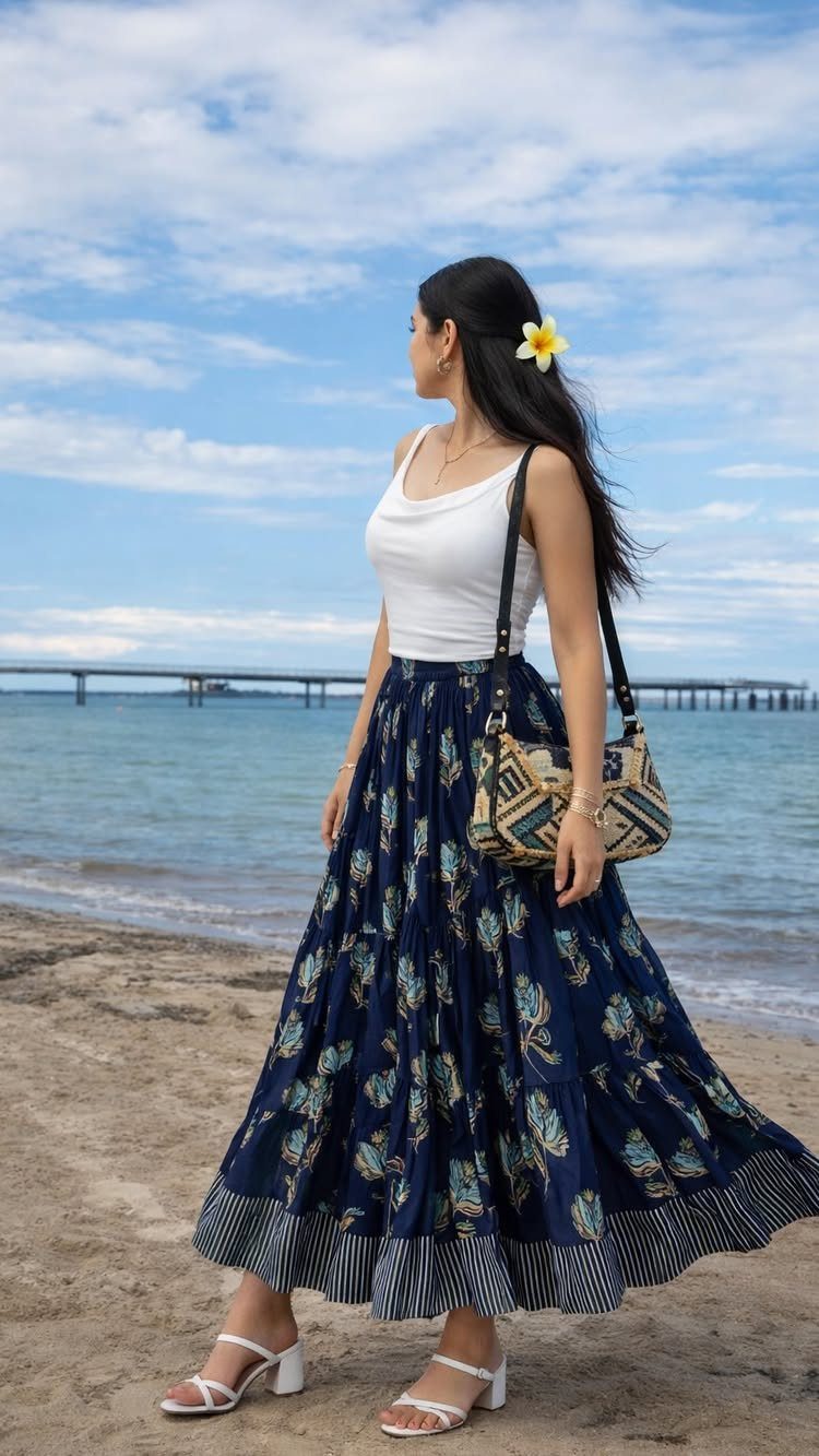 Woman in a white top and long blue patterned skirt standing on a beach.