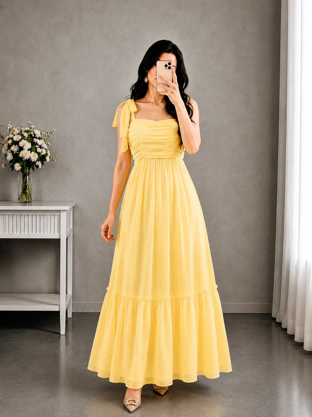 Woman in a long yellow maxi dress taking a mirror selfie in a room.